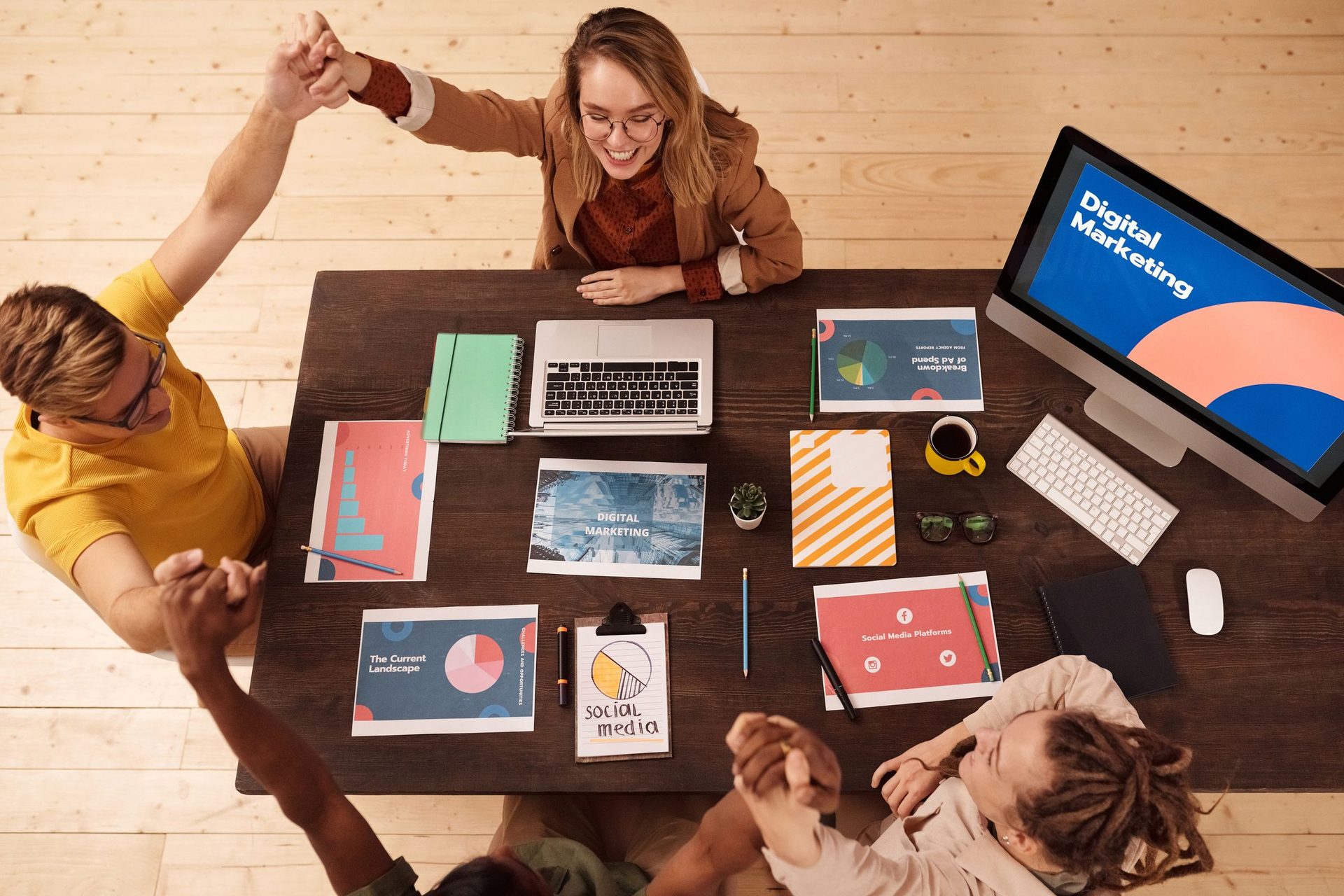 Overhead view of a team high-fiving over a desk of charts and a marketing screen