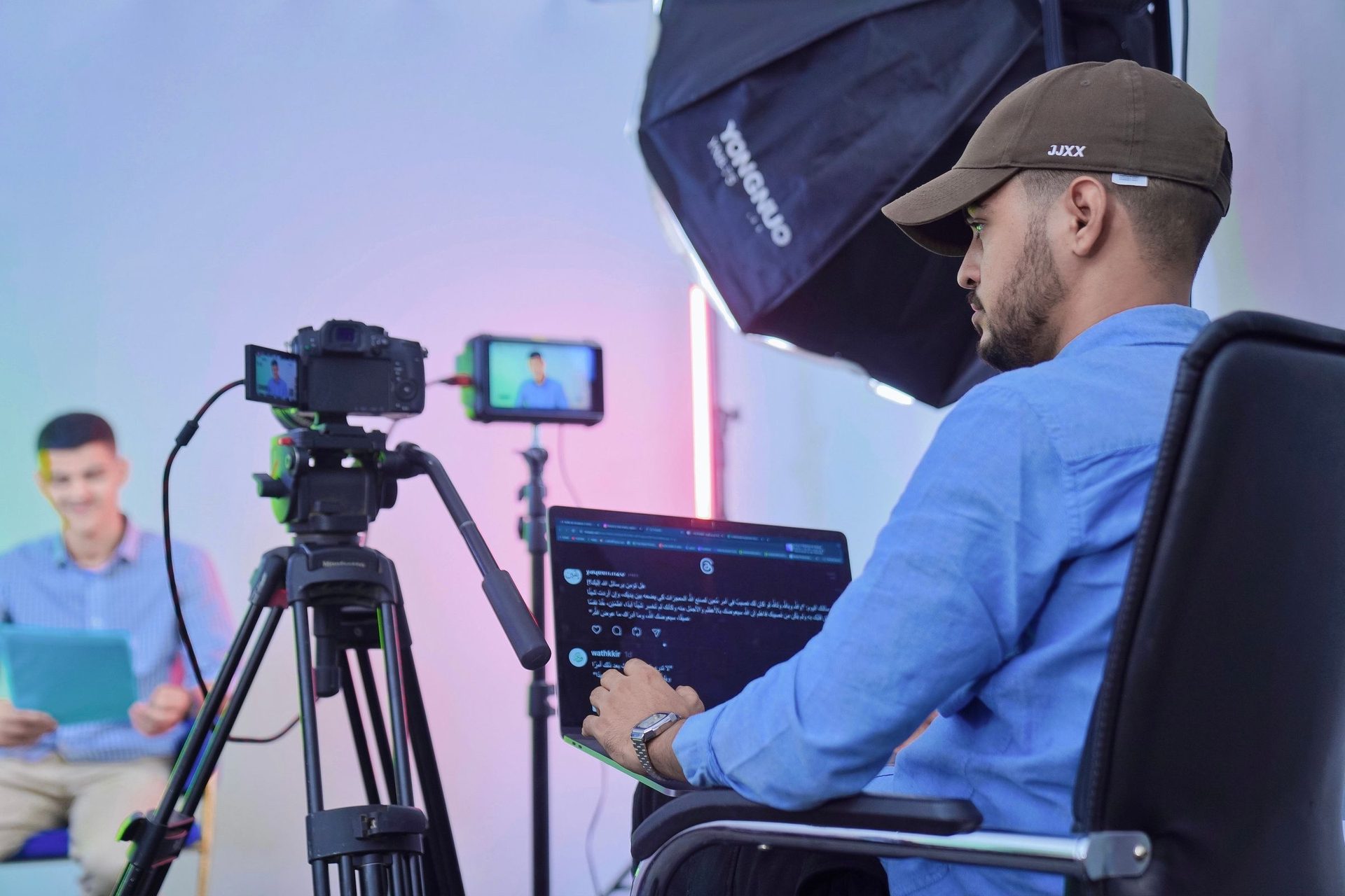 Operator at a laptop runs a tripod camera while a host sits on set
