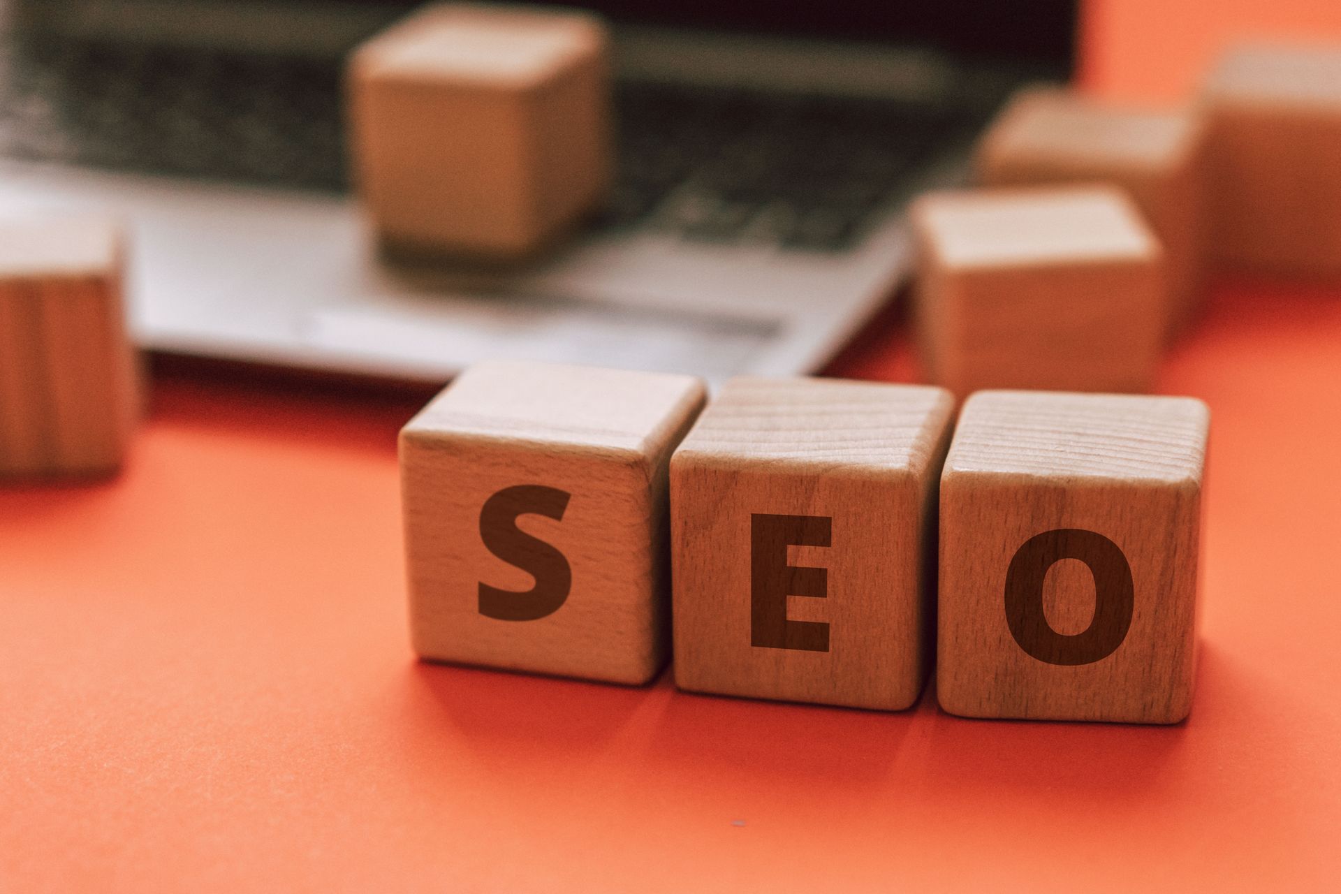 Wooden blocks spelling SEO on an orange desk in front of a laptop