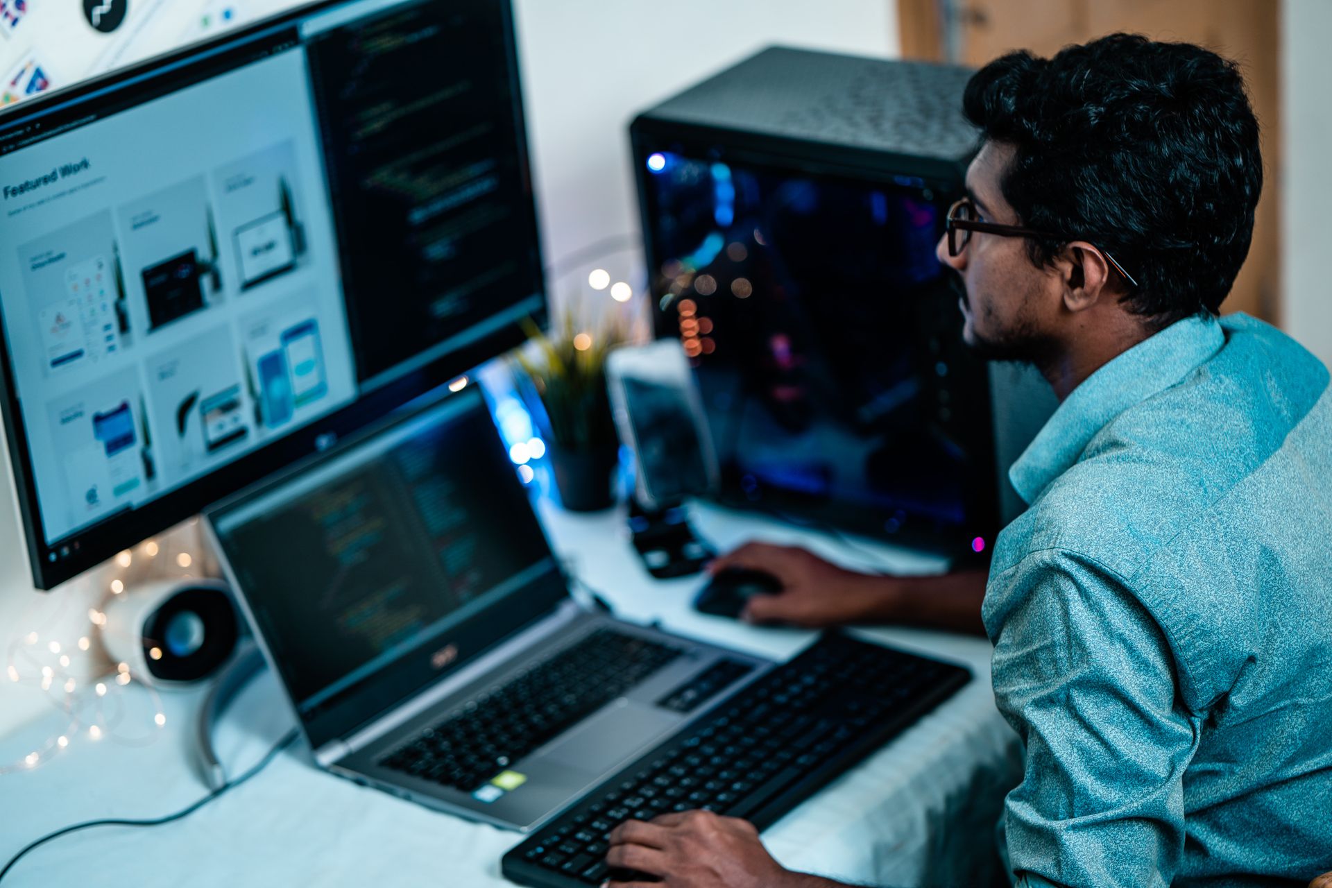 Man at a desk reviewing a web page layout on a monitor beside an open laptop